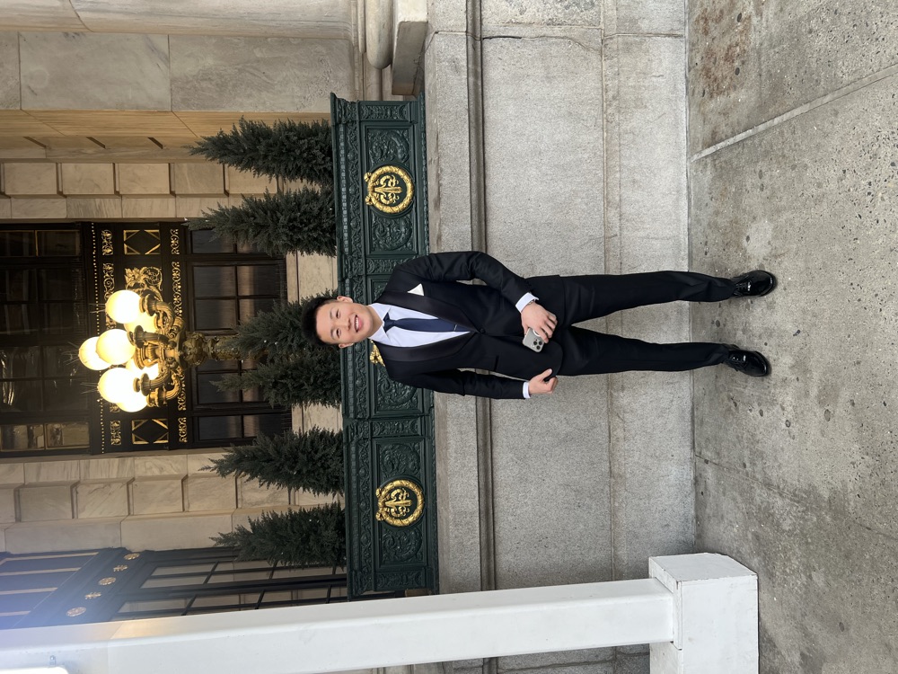 Justin Zhou in formal attire outside a landmark building