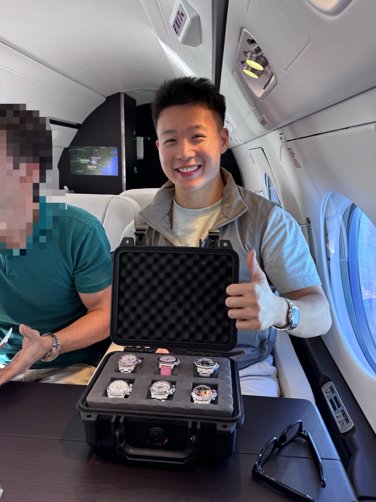 Justin Zhou giving a thumbs up with a case of six watches aboard a private jet